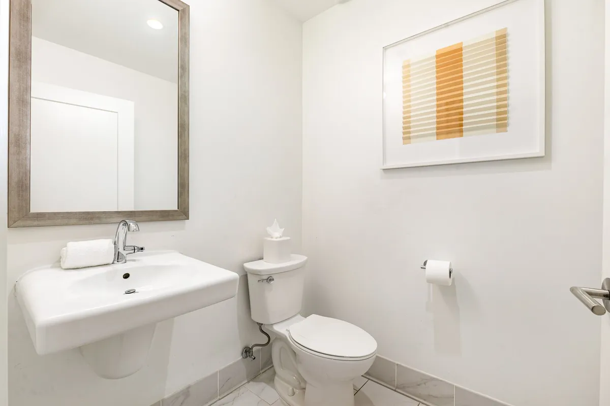 A compact but elegant bathroom with a sink, mirror, modern artwork, and toilet, arranged for both style and convenience.