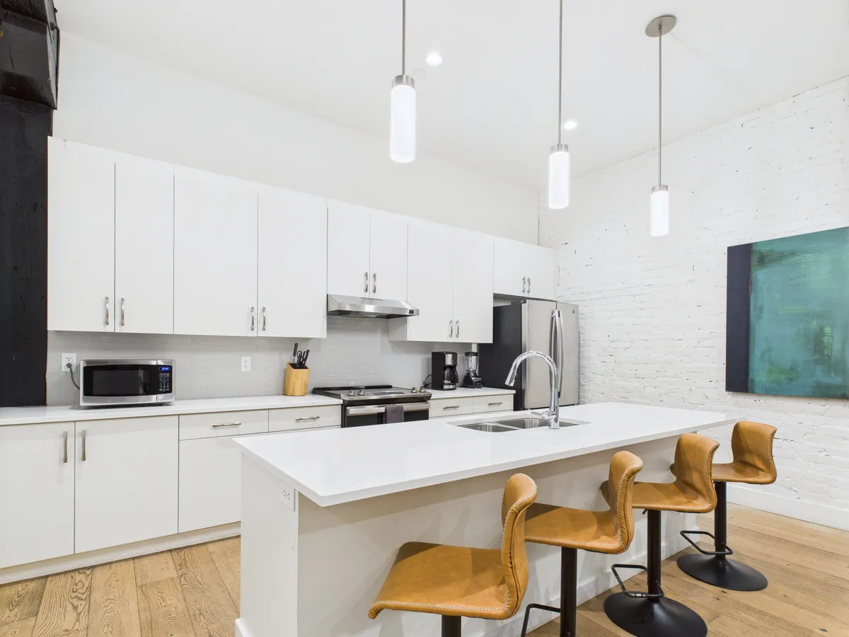 A bright and functional kitchen interior with a prominent kitchen island, bar stools, and artistic wall decor. The layout encourages both cooking and casual dining, underlining the versatility and everyday usability of the space.