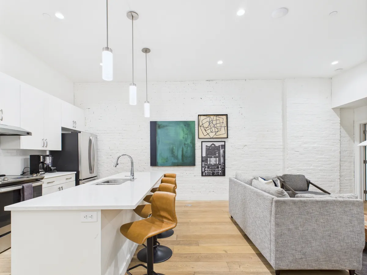 A modern, open-plan space featuring a spacious kitchen island, contemporary artwork on the wall, and a comfortable seating area. High ceilings and industrial-style fixtures highlight the historic and loft-like character. The uncluttered design underscores both the privacy and comfort of the residence, while the visible architectural details evoke the industrial roots of the building.