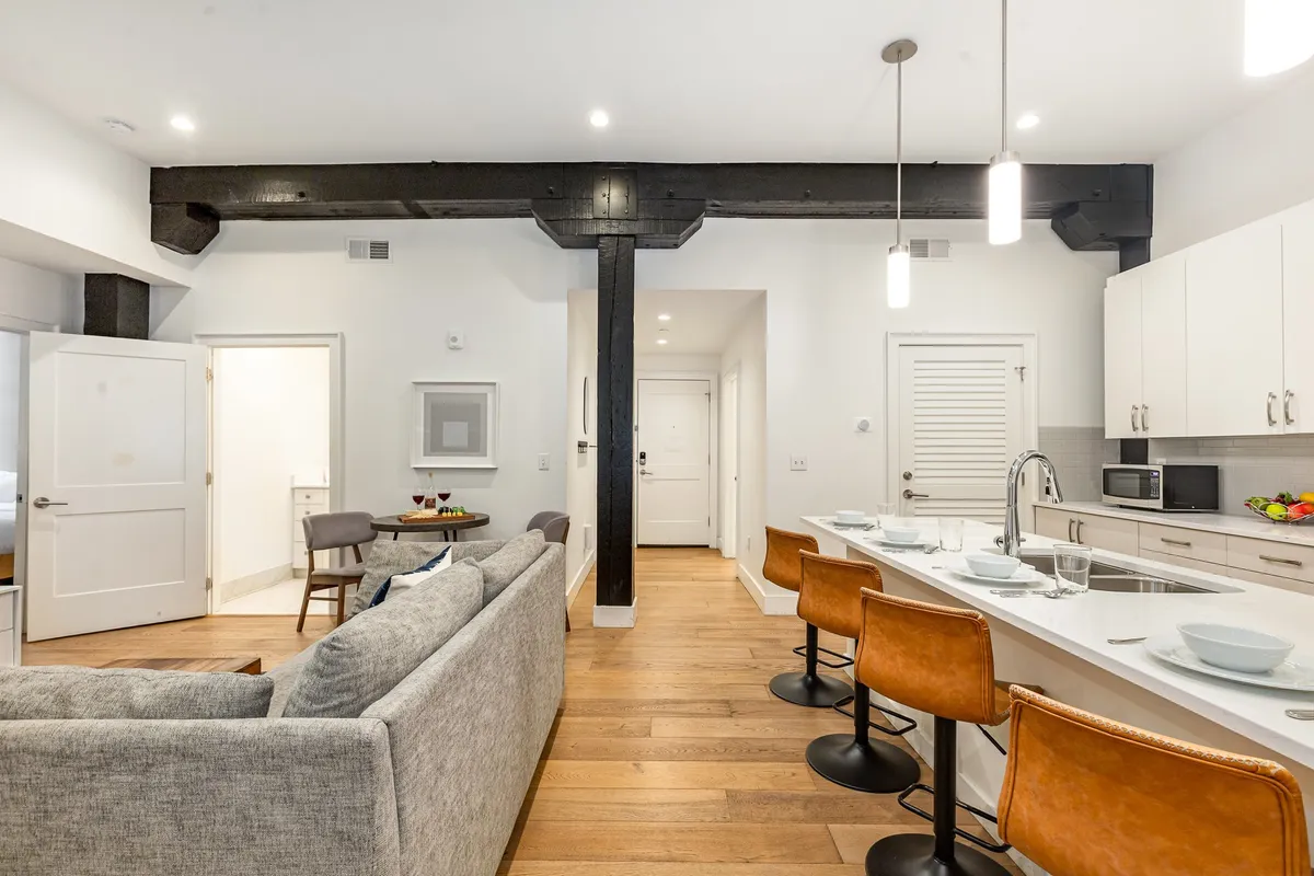 An inviting view of an open-plan kitchen and dining area that includes a kitchen island with bar stools, a visible dining table, and an adjacent cozy living space. The setting is ideal for socializing, cooking, and enjoying meals together, capturing the spirit of casual gatherings.