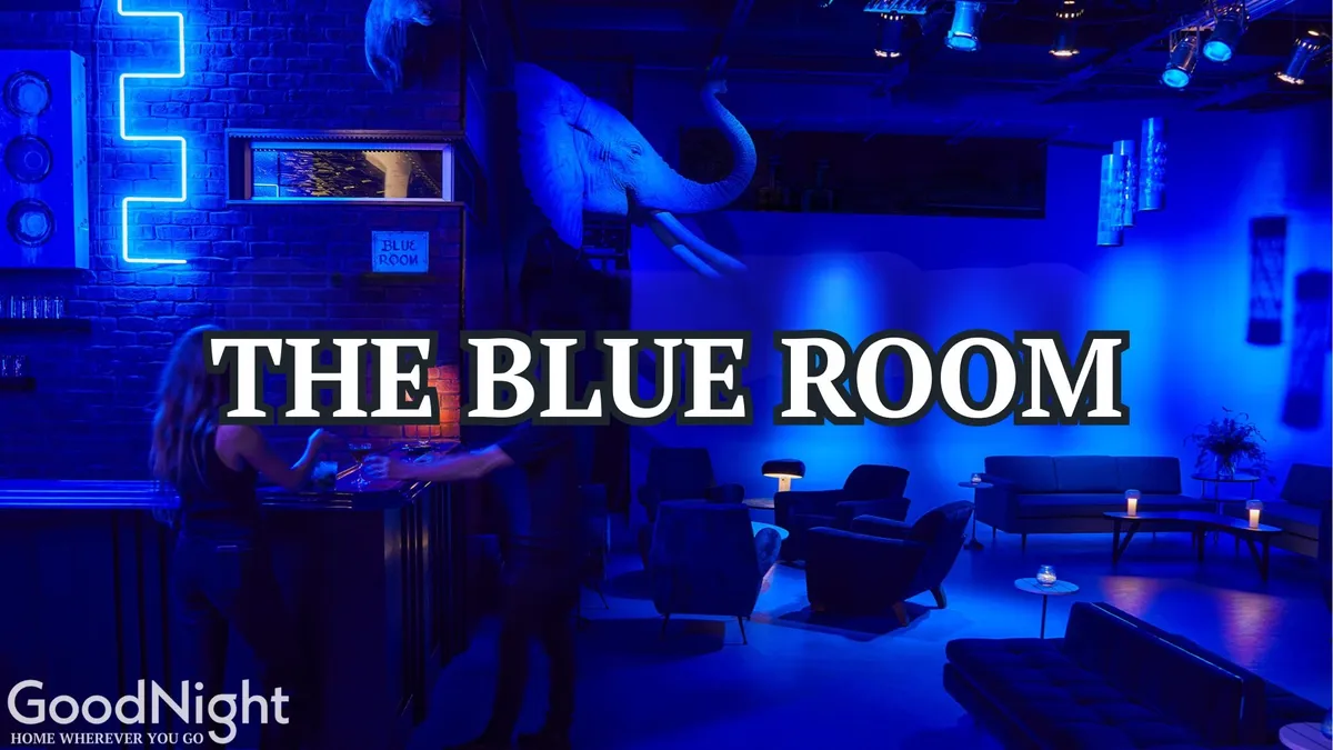 A stylish bar interior illuminated with blue lighting, featuring a cozy seating arrangement and unique decorative elements such as an elephant statue. The setting is intimate, perfect for sharing cocktails and conversation in a sophisticated lounge atmosphere.